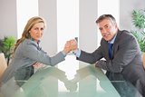 Two serious businesspeople having an arm wrestling sitting around a table