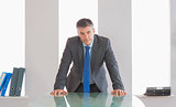 Frowning businessman standing in front of a desk