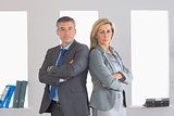 Two unsmiling businesspeople looking at camera standing back to back with crossed arms