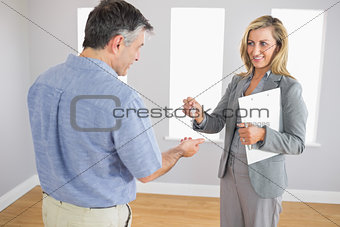 Pleased realtor holding a briefcase and giving a key to a buyer