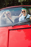Mature couple in red cabriolet smiling at camera