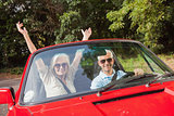 Mature couple in red cabriolet cheering at camera