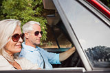 Side view of mature couple driving red cabriolet