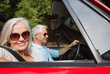 Side view of smiling mature couple driving red cabriolet