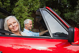 Side view of mature couple driving red convertible