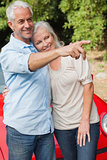 Smiling mature couple posing by their red convertible