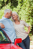 Smiling mature couple leaning against their red cabriolet