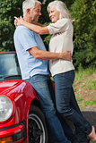 Happy mature couple hugging against their red cabriolet
