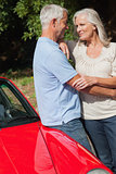 Cheerful mature couple hugging against their red cabriolet