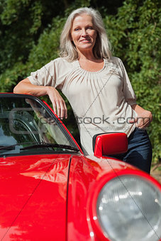 Smiling mature woman leaning against her red cabriolet