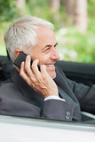 Cheerful mature businessman on the phone driving expensive cabriolet