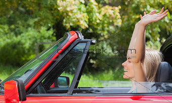 Happy blonde woman enjoying her red cabriolet