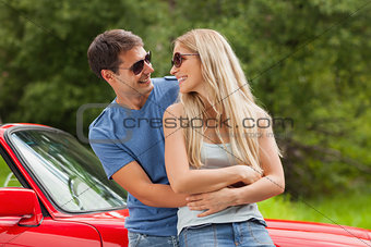 Cheerful young couple hugging and leaning against cabriolet
