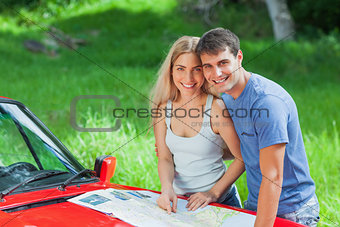 Happy young couple reading map on their cabriolet bonnet