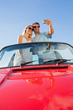 Smiling couple standing in red cabriolet taking picture