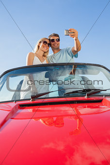 Smiling couple standing in red cabriolet taking picture