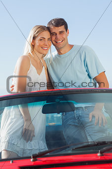 Smiling couple standing in red cabriolet posing