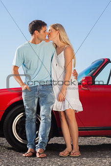 Cute couple kissing against their red cabriolet