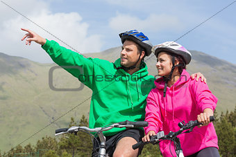 Smiling couple on a bike ride wearing hooded jumpers with man pointing