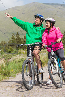Athletic couple on a bike ride wearing hooded jumpers with man pointing