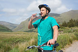 Fit man leaning on his mountain bike drinking water