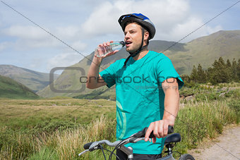 Fit man leaning on his mountain bike drinking water