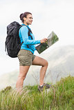 Attractive hiker with backpack walking uphill holding a map
