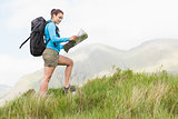 Attractive hiker with backpack walking uphill reading a map