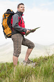 Handsome hiker with rucksack walking uphill holding a map