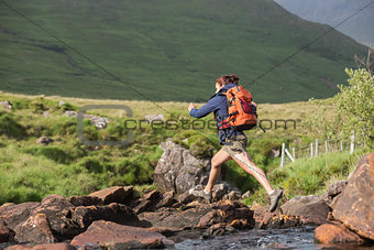 Athletic hiker leaping across rocks in a river