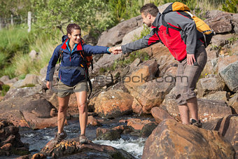 Man helping his smiling girlfriend to cross a river