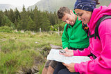 Couple sitting on a rock resting during hike using map and compass