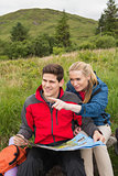 Cheerful couple taking a break on a hike to look at map with woman pointing