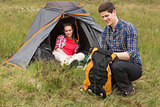 Happy man packing backpack while girlfriend sits in tent