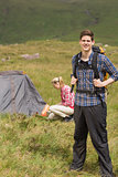 Happy man carrying backpack while girlfriend is pitching tent