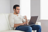 Relaxed attractive man holding coffee while working on his laptop