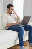 Relaxed attractive man drinking coffee while working on his laptop