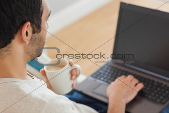 Handsome man drinking coffee while using his laptop
