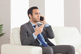 Serious businessman on the phone sitting on cosy sofa