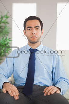 Serious classy businessman sitting on cosy sofa