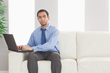 Stern businessman using his laptop while sitting on cosy sofa