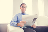 Pleased man looking at camera and holding a newspaper sitting on a sofa