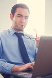 Irritated man biting his eyeglasses and using a laptop