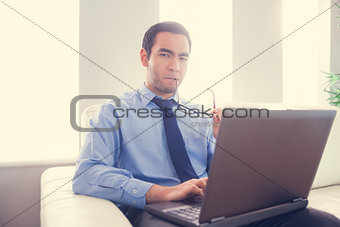 Nervous man biting his eyeglasses and using a laptop