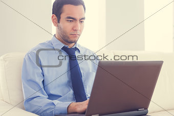 Stern man using a laptop sitting on a sofa