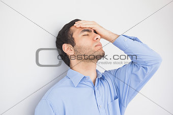 Irritated man with hand on forehead leaning against a wall