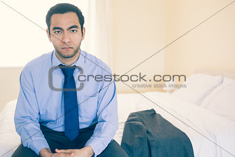 Frowning man looking at camera sitting on his bed