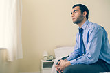 Thinking man looking away sitting on his bed