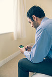 Man using a mobile phone sitting on a bed