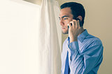 Irritated man calling someone with a mobile phone and looking out the window
